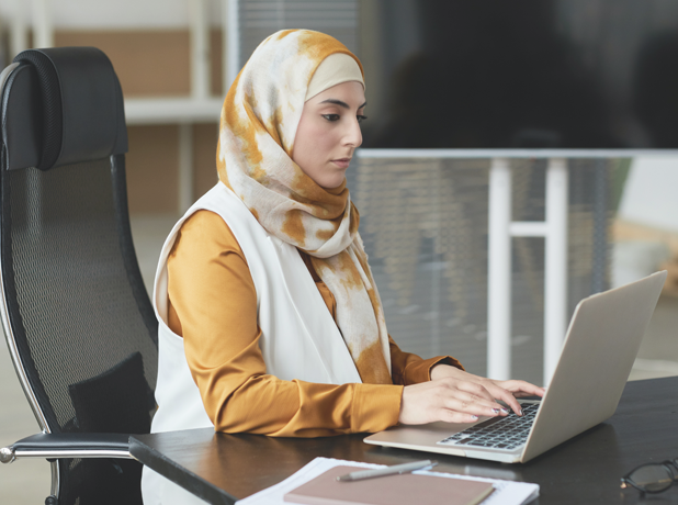 EST -BodyImageModule-pexels-618x460px Portrait of female wearing hijab sitting at a computer desk studying.