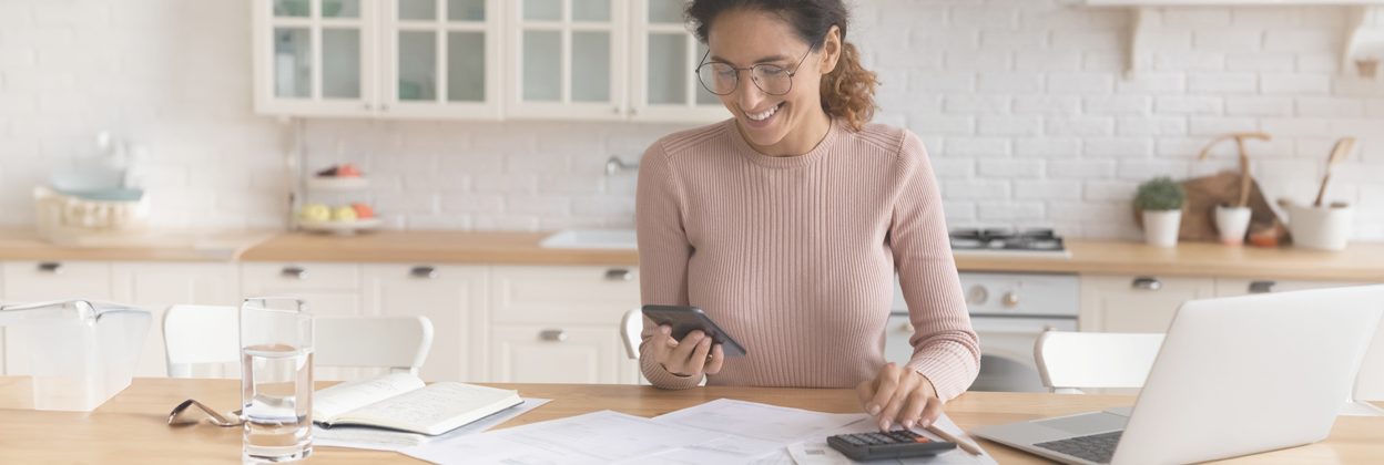 EST-CampaignHeaderBanner-istock1415850959-1248x420px Young 30s Latina woman sitting at kitchen counter working out EST Course payments.