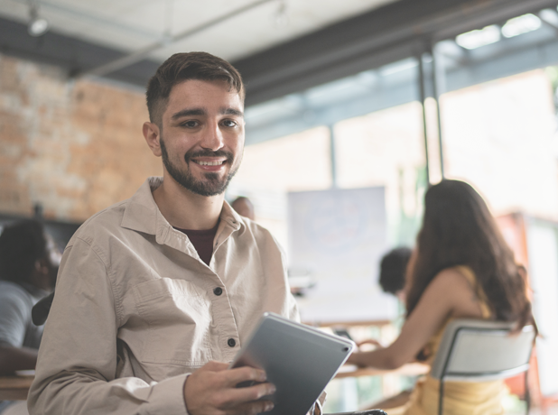 NDIS - Full Image - Media and Text Split 618x460px_iStock-1368083626v2 Young man in office looking at the camera and smiling.<br />