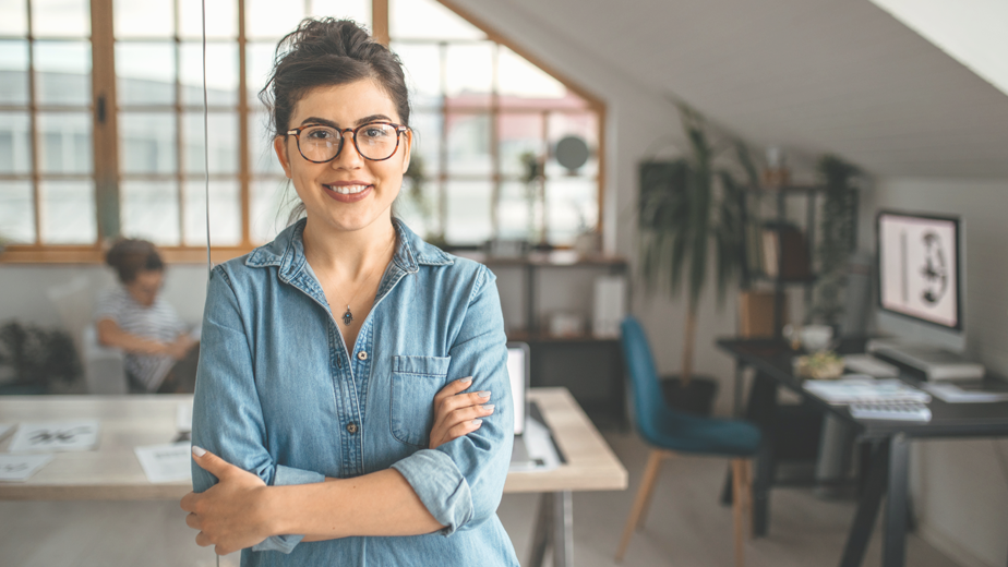 NILS-ProgramHeaderBanner-924x520px-iStock-1350738281 Portrait of young smiling woman in creative office, standing with arms crossed, looking at camera.