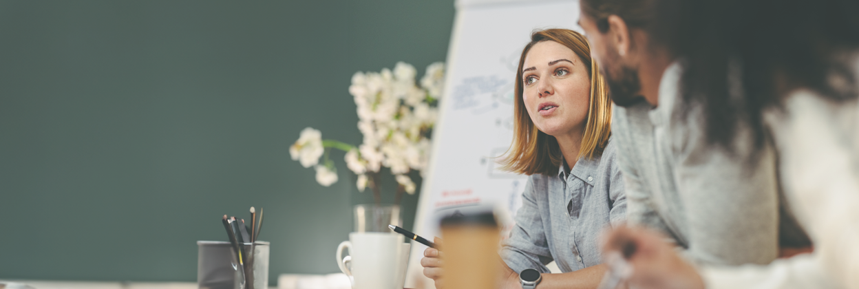 SS - Campaign Header Banner -1248x420px - Complaints - July24 A beautiful young woman sits speaking to her colleagues in a meeting.