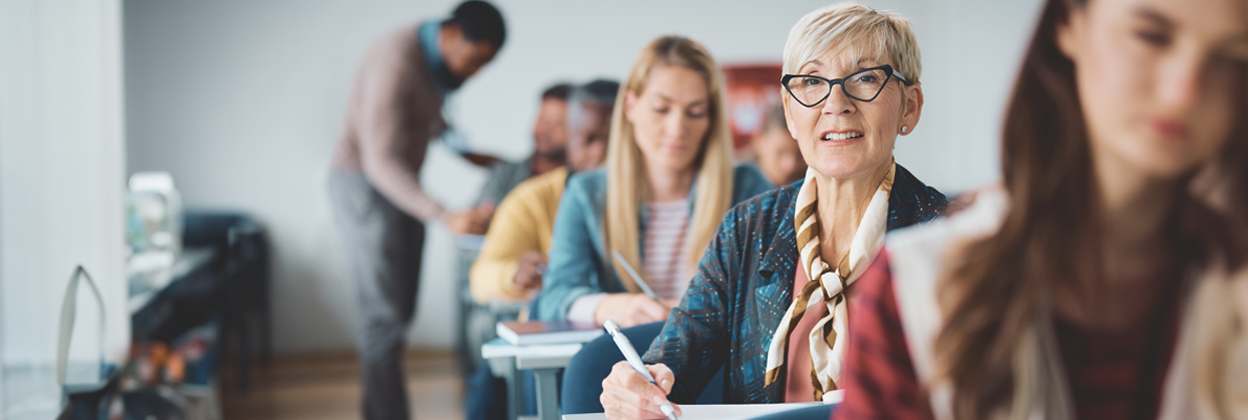 CTA -CampaignHeaderBanner-iStock-1614142973-858x643px-updated Mature female student taking notes while attending a course in lecture hall.