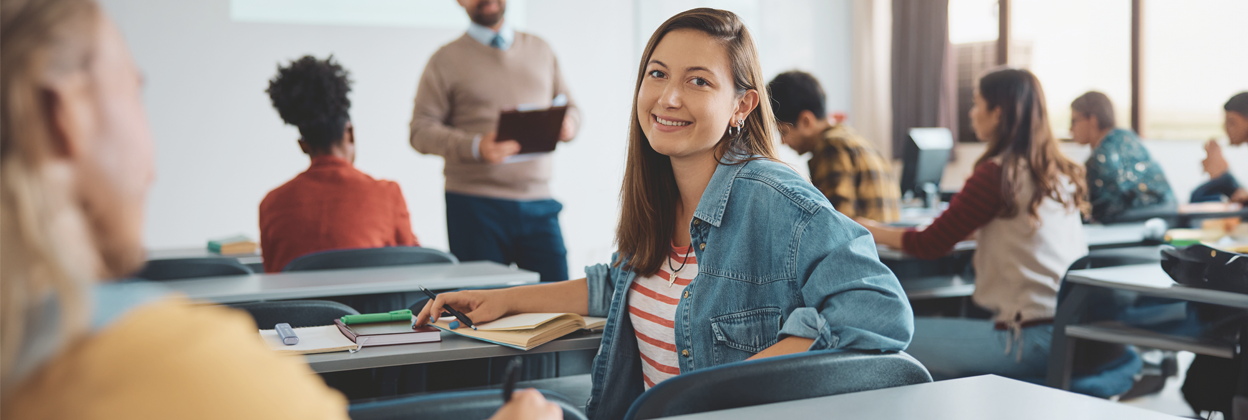 CampaignLandingPageBanner-iStock-1588289438-1248x420px2 Adult female student, turning around and looking to camera smiling in a classroom environment.