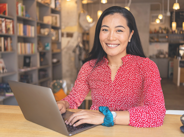 EST -BodyImageModule-iStock-1344252956-618x460px Asian woman sitting at a table in a library on her laptop.