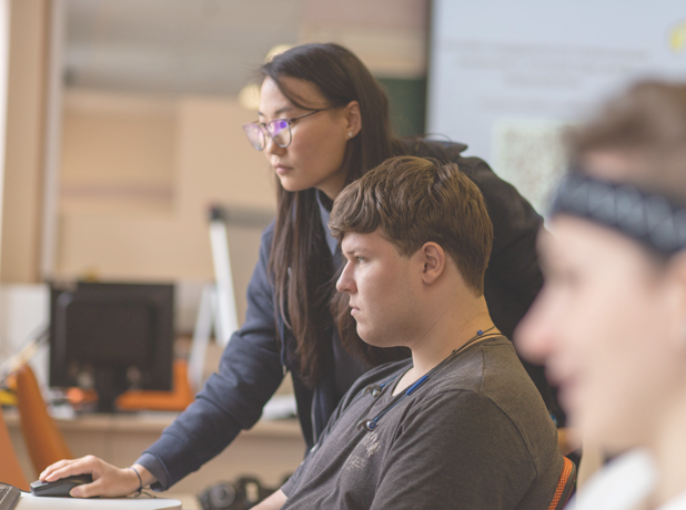 Generic -BodyImage-pexels-12197305-618x460 Teacher helping students on a computer in a classroom setting.