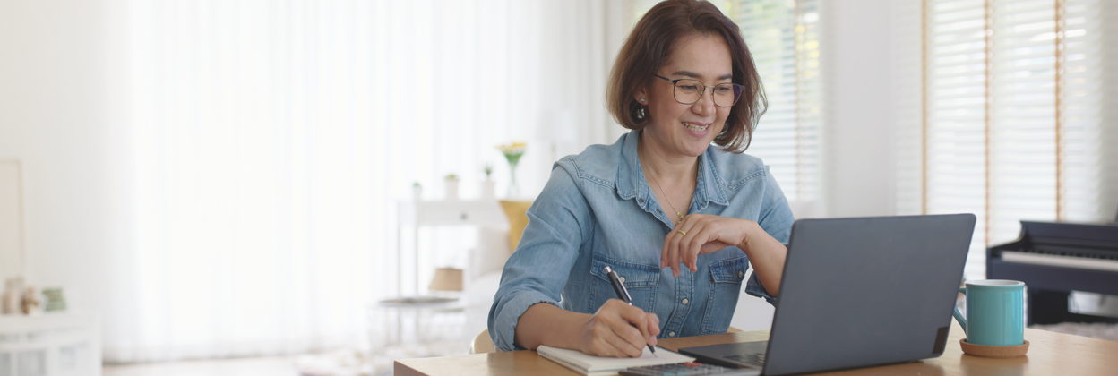 SEA-CampaignHeaderBanner-iStock-1345356877-1248x420px Asia happy female adult at desk looking at laptop while writing and working on her small business.