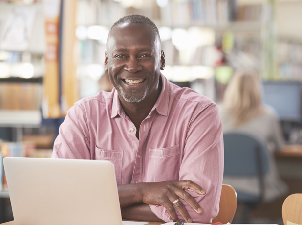 SEA - Full Image - Media and Text Split 618x460px_15c Portrait of bald, African Aerican mature male using laptop In Library