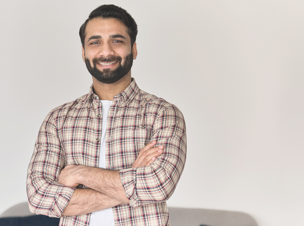 SEE -BodyImageModuleiStock-1310078148-618x460px Portrait of young happy indian business man looking at camera standing with arms crossed at home office.