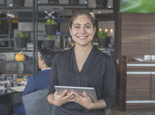SEE - Full Image - Media and Text Split 618x460px_10c Hispanic waitress standing and smiling to camera holding touchpad at a high-class restaurant.