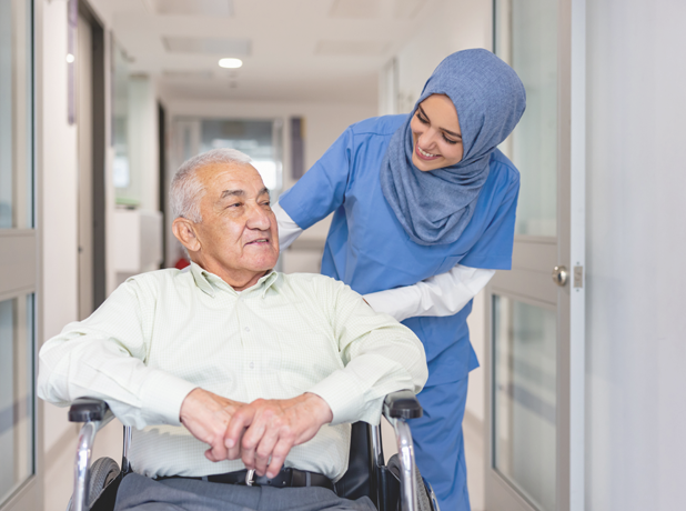 SEE - Full Image - Media and Text Split 618x460px_9c Female, Muslim aged-care worker smiling and looking down at elderly man whilst pushing his wheelchair.