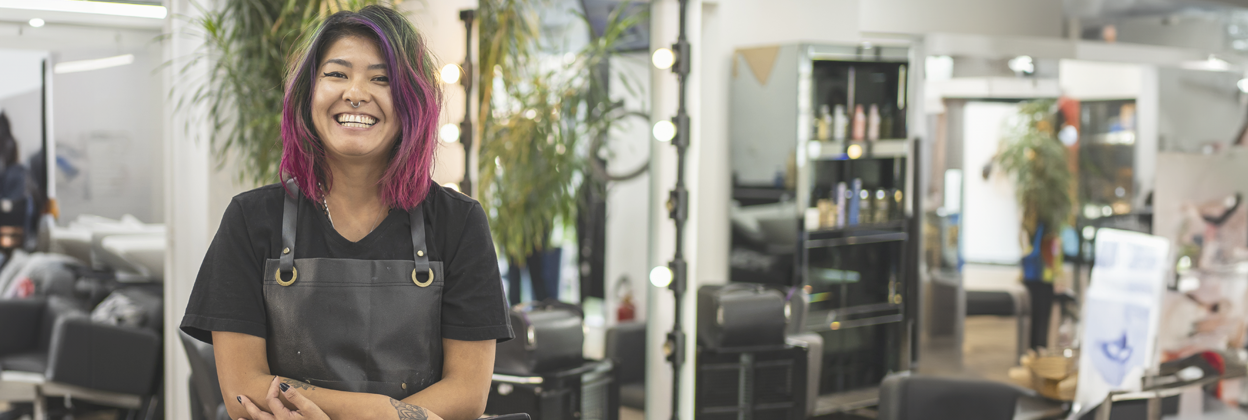 VET-CampaignHeaderBanner-iStock-1398386378-1248x420px Portrait of Asain female hairdresser with pink dyed hair at hair salon holding scissors.