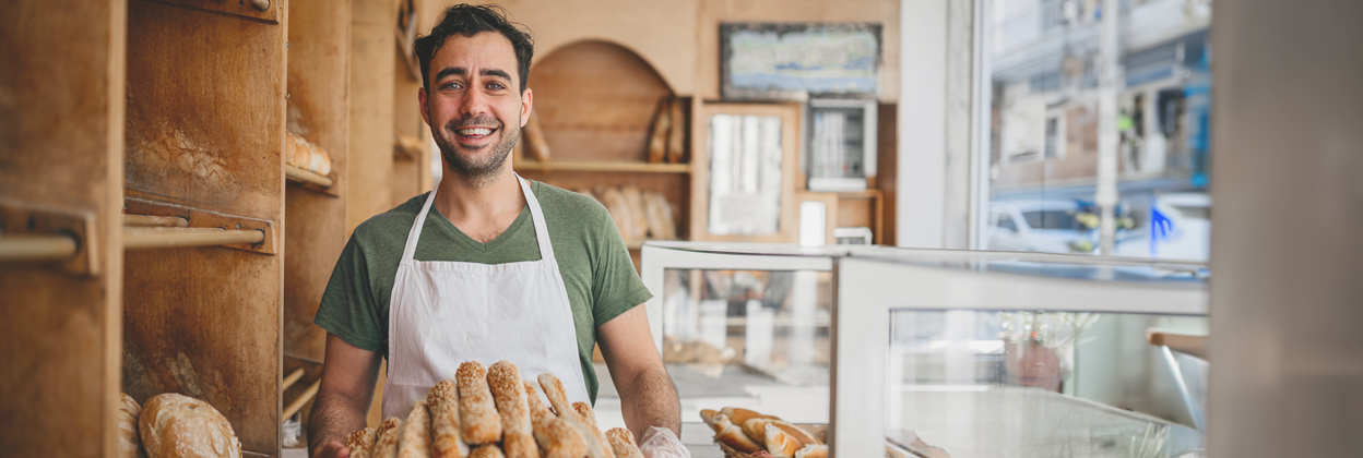 Male baker holding a basket of fresh bread in his bakery business. 