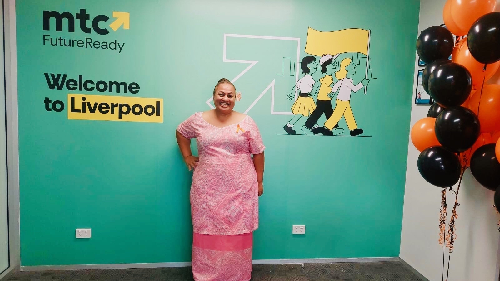 Amanda wearing traditional Samoan clothing and standing in front of a wall with MTC FutureReady logo 